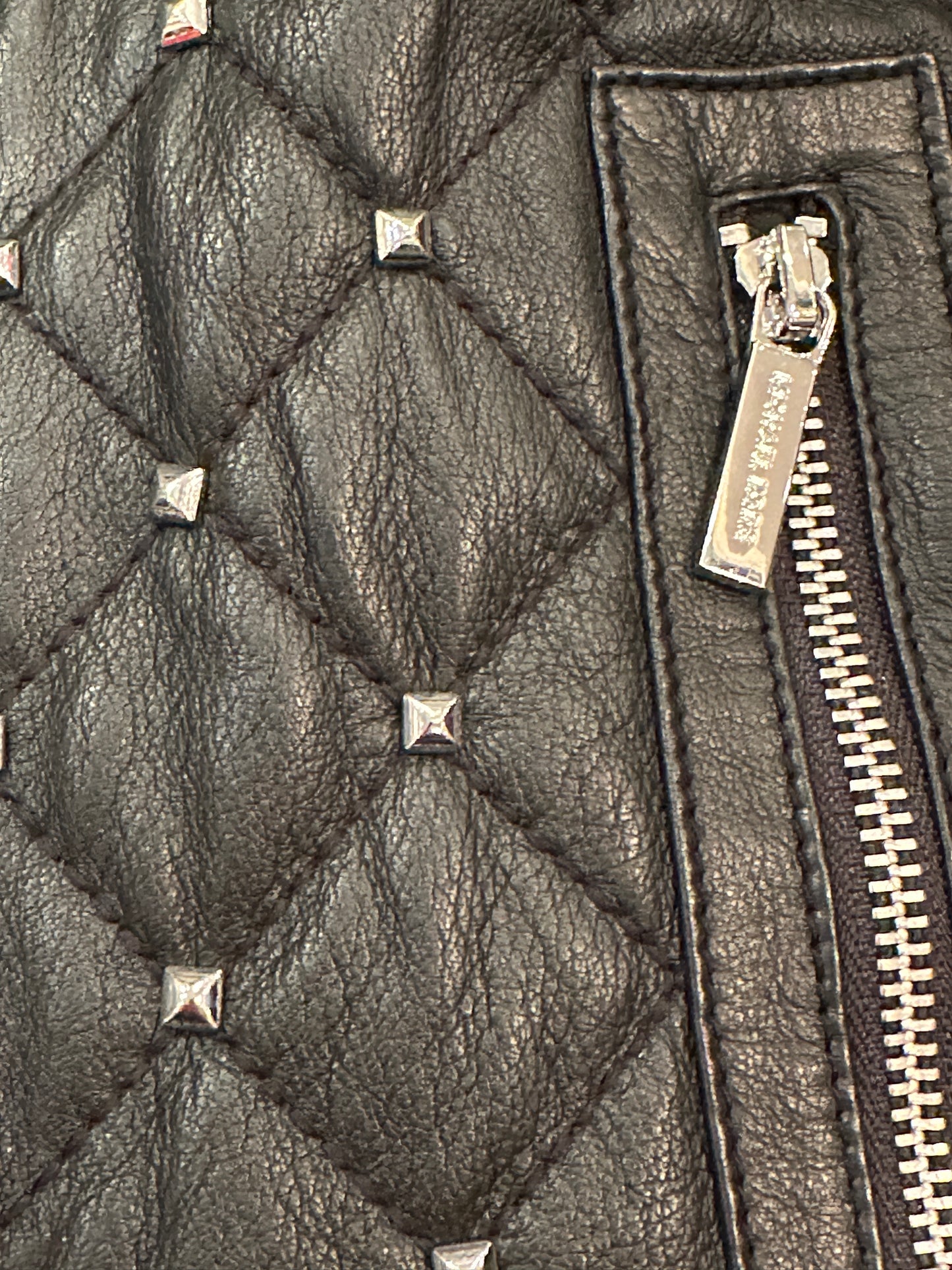 Close-up of Michael Kors leather jacket showcasing quilted texture and silver nail decorations.