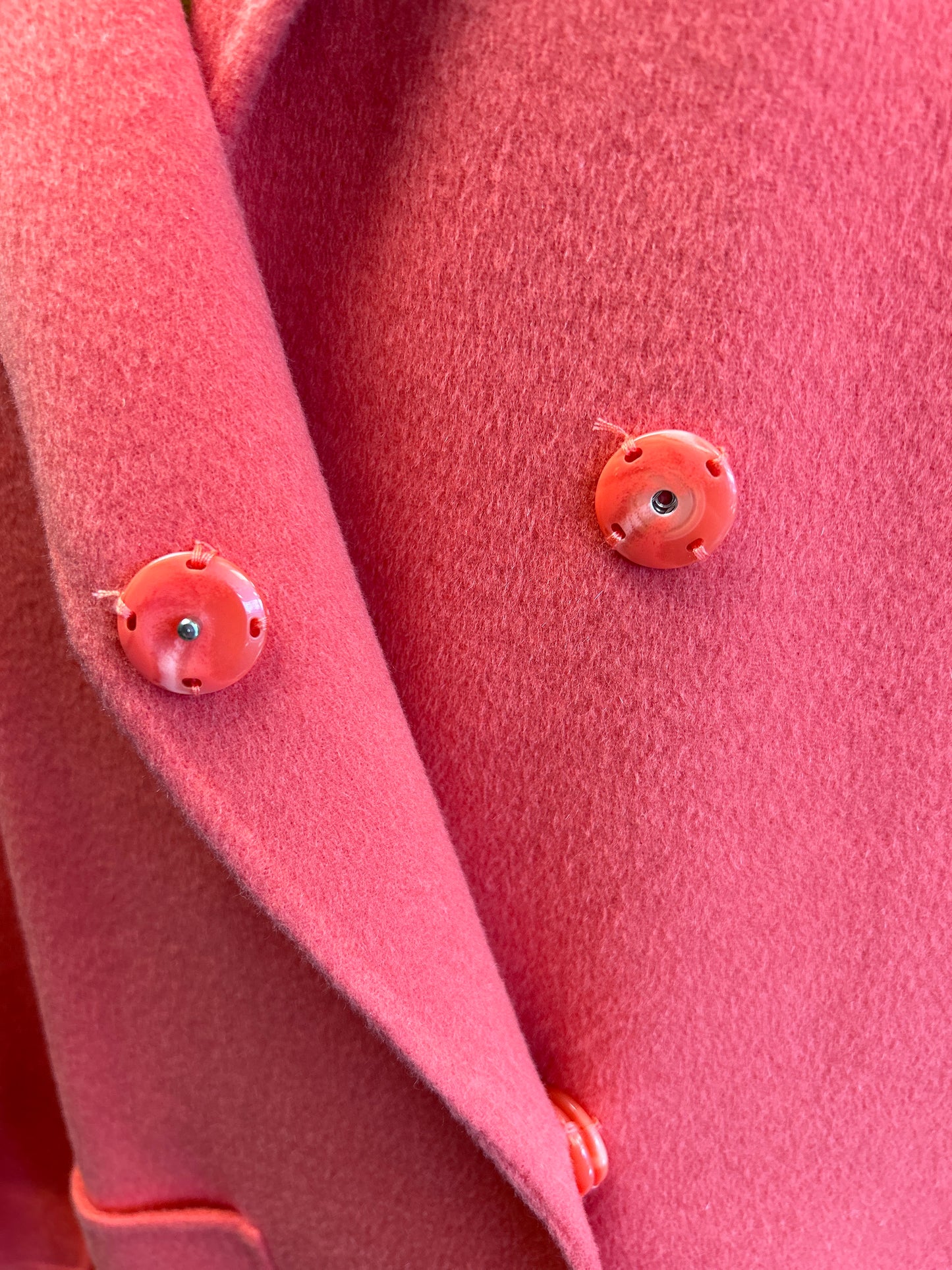 Close-up of Marccain coral red long coat detail featuring stylish buttons and soft fabric texture.