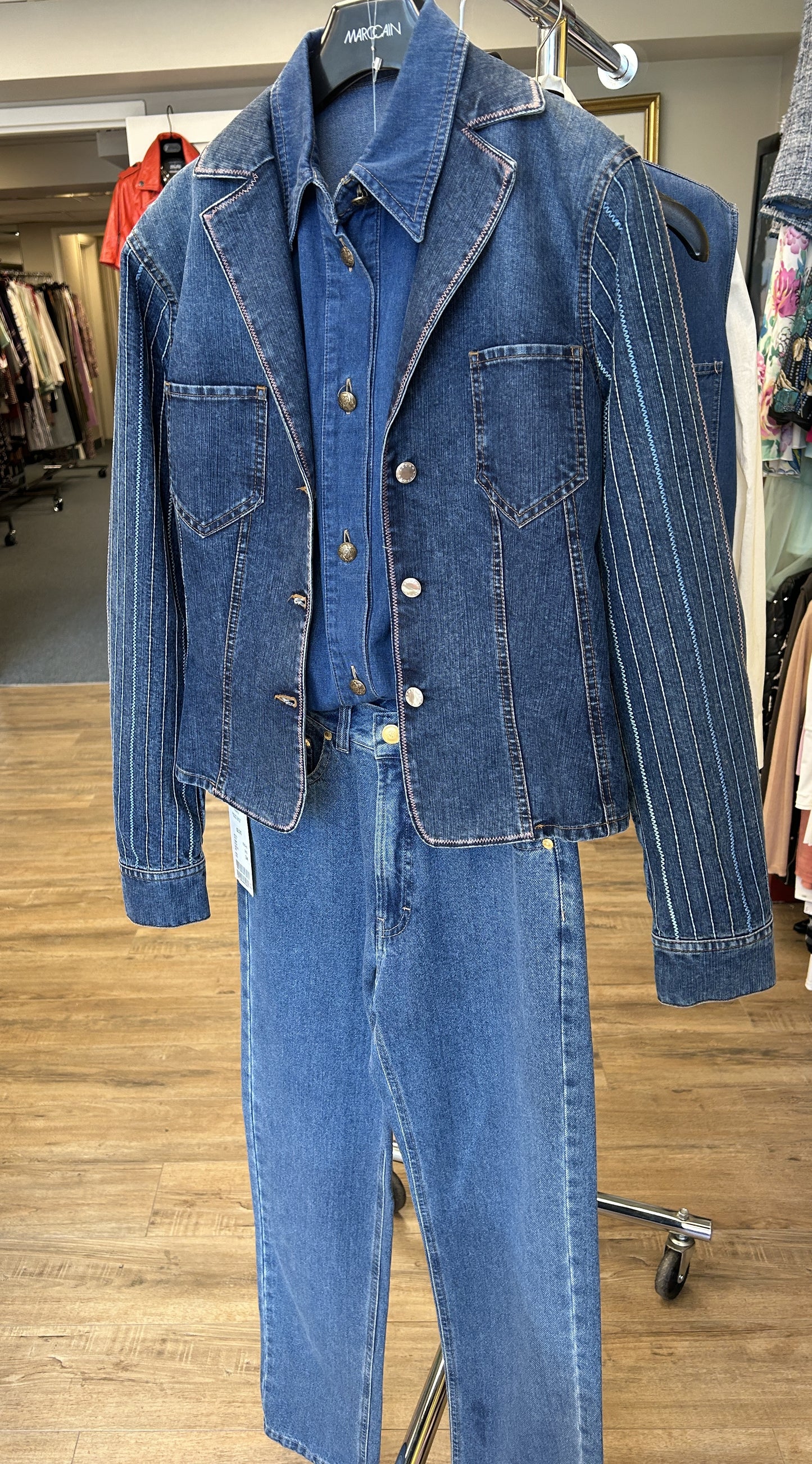 Escada denim jacket with stylish tailored collar, intricate stitches, displayed with matching denim pants on a hanger.