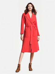 Model showcasing a Marccain coral red long coat with pockets and a belt, paired with brown lace-up boots.