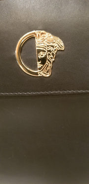 Close-up of Versace black handbag featuring iconic gold logo, showcasing luxury craftsmanship.
