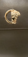 Close-up of Versace black handbag featuring iconic gold logo, showcasing luxury craftsmanship.