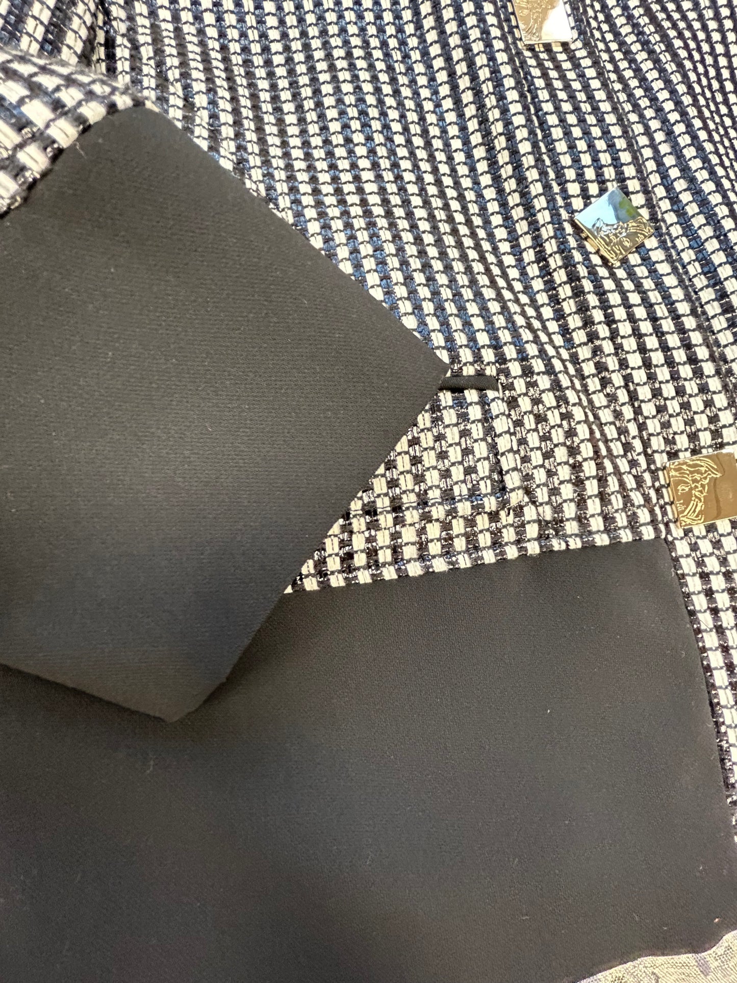Close-up of Versace black and white checked jacket fabric and cuff detail, showcasing elegant design elements.