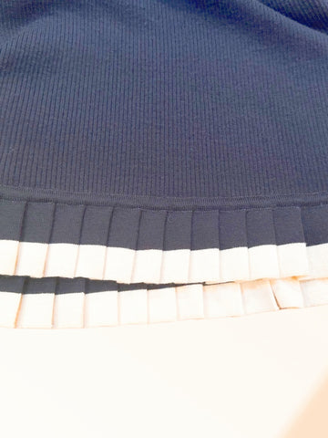 Close-up of the hemline of a black wool dress featuring a pleated white trim, showcasing its elegant design details.
