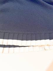 Close-up of the hemline of a black wool dress featuring a pleated white trim, showcasing its elegant design details.