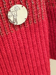 Close-up of a bold red Versace sweater featuring a silver emblem and gold threading design.