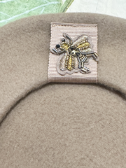 Close-up of a beige wool beret with intricate insect beading decoration, showcasing quality craftsmanship.