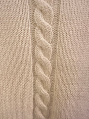 Close-up of a Versace white sweater showcasing the intricate green thread braid along the sleeves.