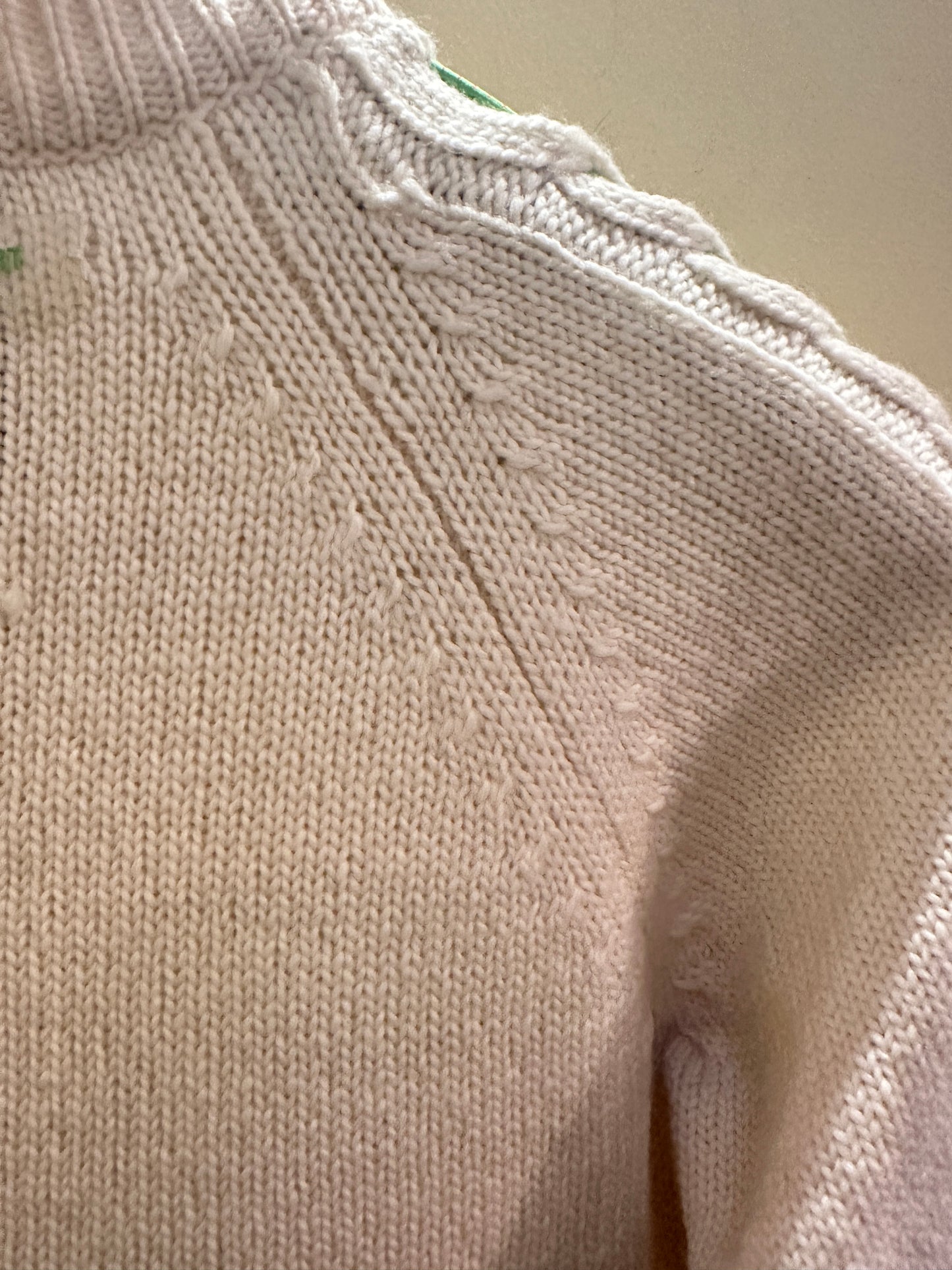 Versace white sweater detail showing sophisticated knit texture and green thread braid design.