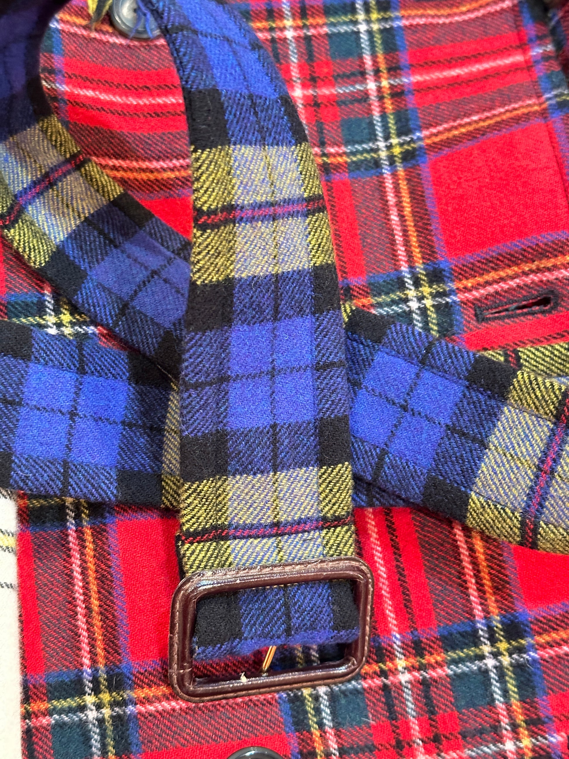 Close-up detail of a Moschino tartan coat featuring colorful plaid fabric and a stylish buckle.