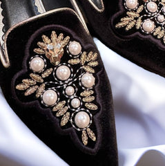 Close-up of Marccain black slip-on flats featuring elegant pearl and gold thread embellishments.
