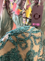 Close-up of Save The Queen green dress showcasing intricate textures and vibrant floral patterns.