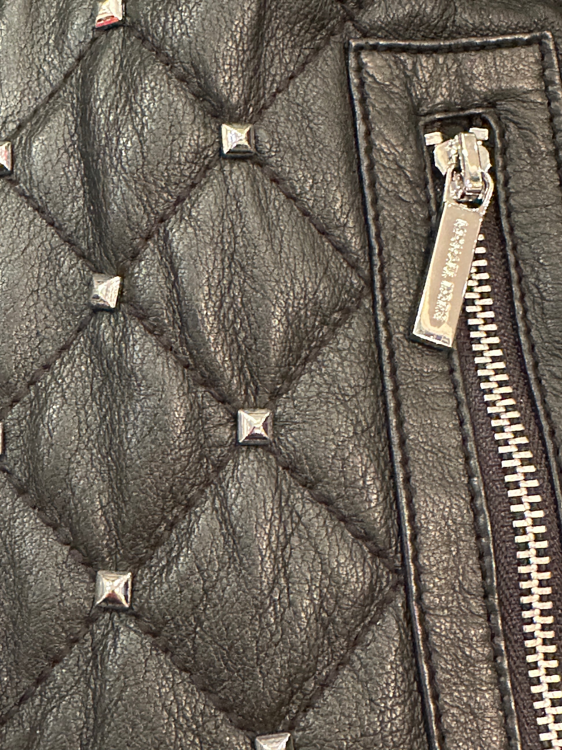 Close-up of Michael Kors leather jacket showcasing quilted texture and silver nail decorations.
