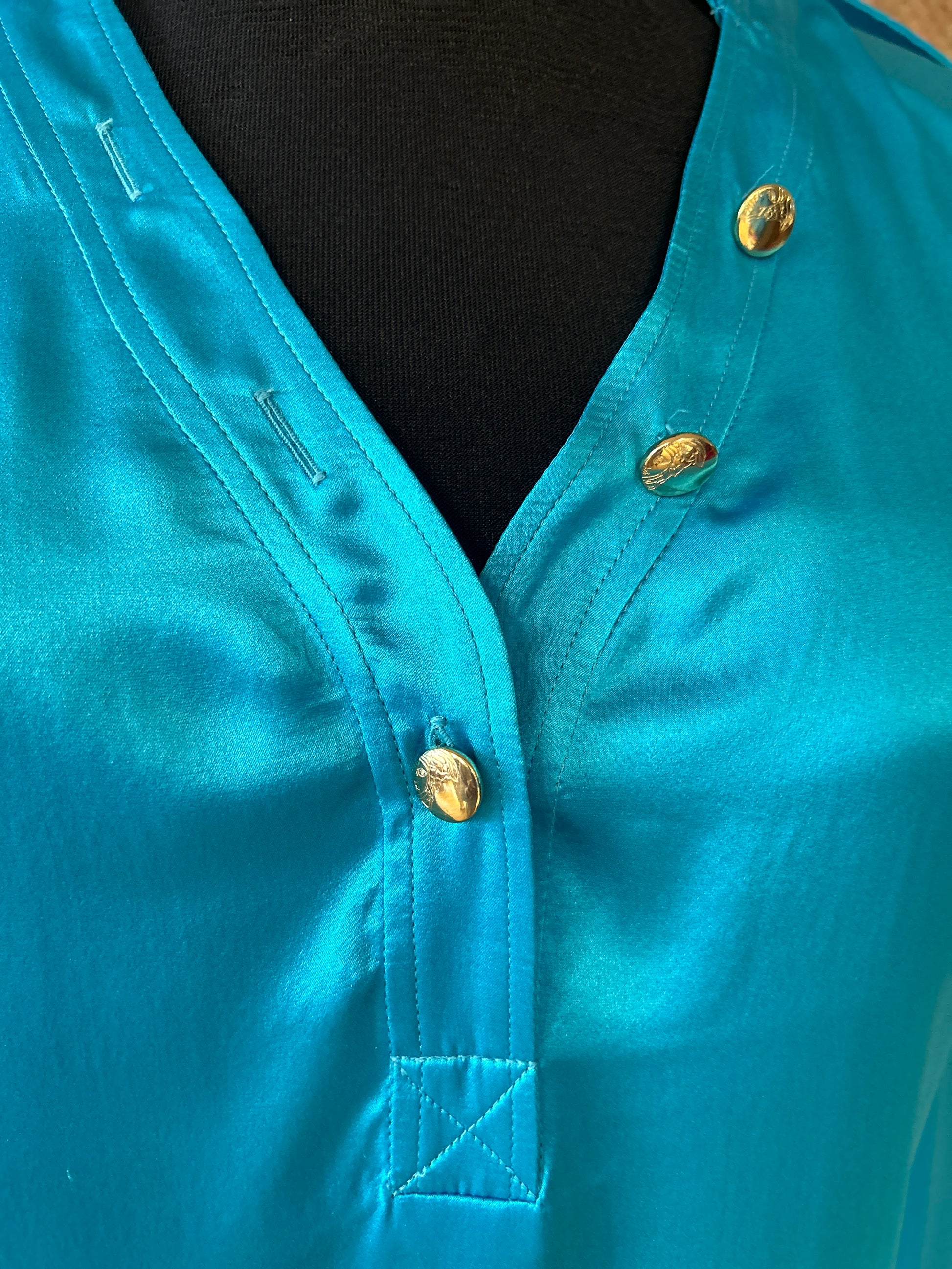 Close-up of Versace silk shirt in vibrant turquoise, featuring elegant buttons and luxurious fabric texture.