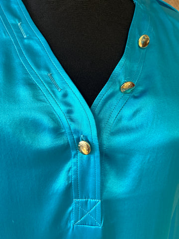 Close-up of Versace silk shirt in vibrant turquoise, featuring elegant buttons and luxurious fabric texture.