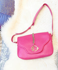 Versace leather bag in vibrant pink with adjustable strap and decorative clasp, placed on a soft white background.