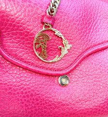 Close-up of a pink Versace leather bag featuring a gold logo charm and textured leather surface.