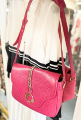 Stylish pink leather handbag with chain detail, hung beside a white and black sweater in a boutique setting.