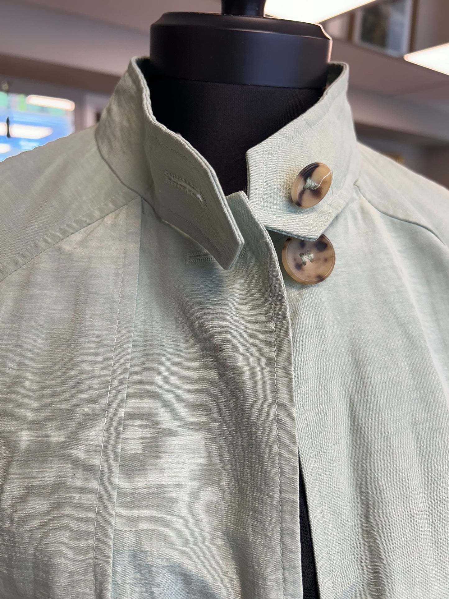 Close-up of Nic Janik Green Linen Coat featuring two style collars and buttons, showcasing its light green color and linen texture.