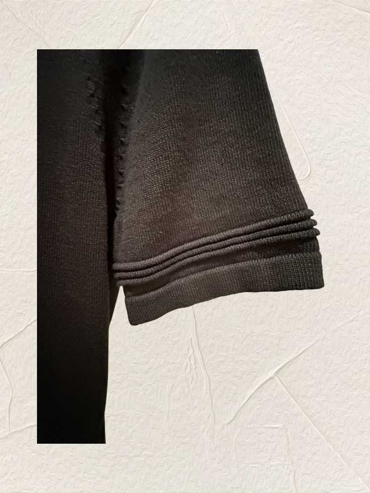 Close-up of a black sweater sleeve showcasing knit texture and detailing, ideal for casual or formal wear.