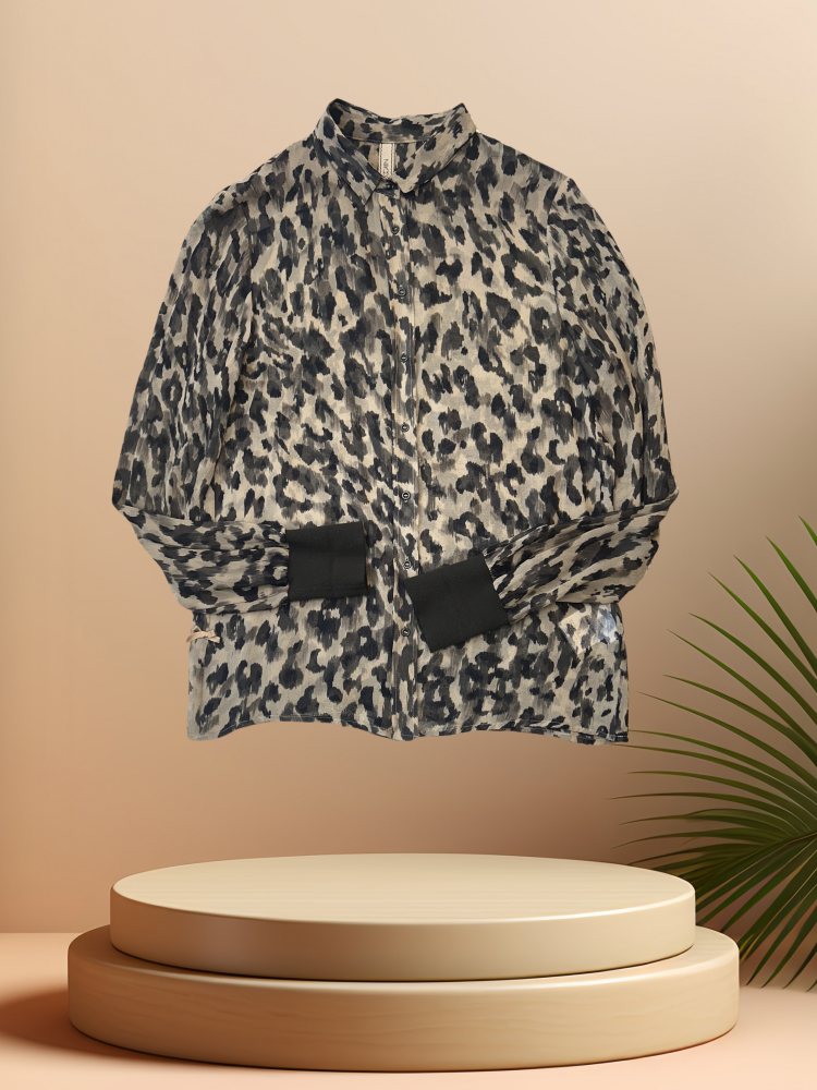 Marccain Silk Leopard Print Shirt displayed on a pedestal with palm leaves, showcasing its chic design and quality fabric.