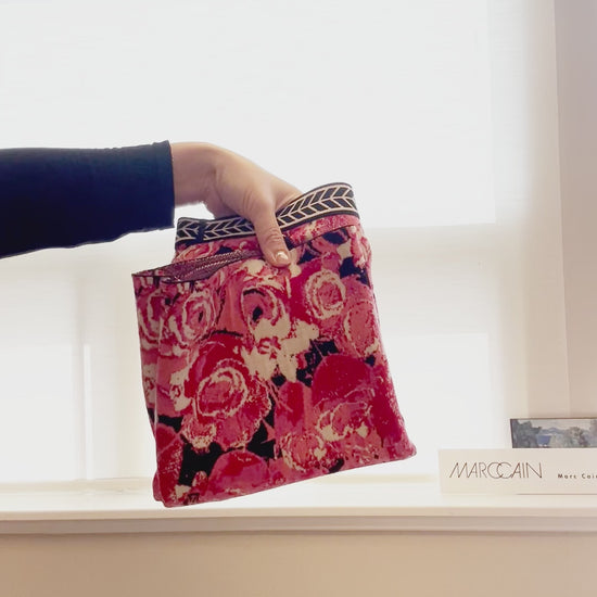 Hand holding a Marccain pink floral print bag, showcasing its stylish design and vibrant rose pattern.